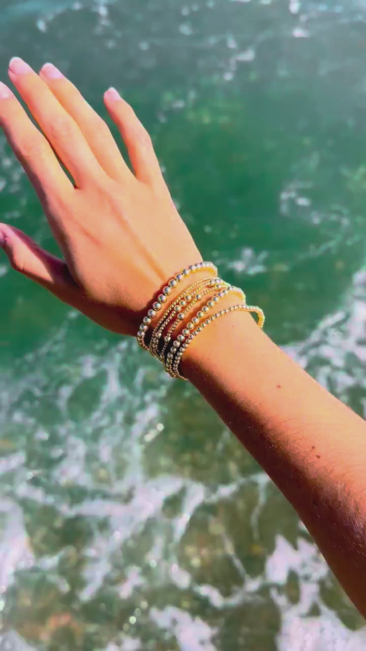 Stack of Steadfast gold-filled bracelets in ocean surf