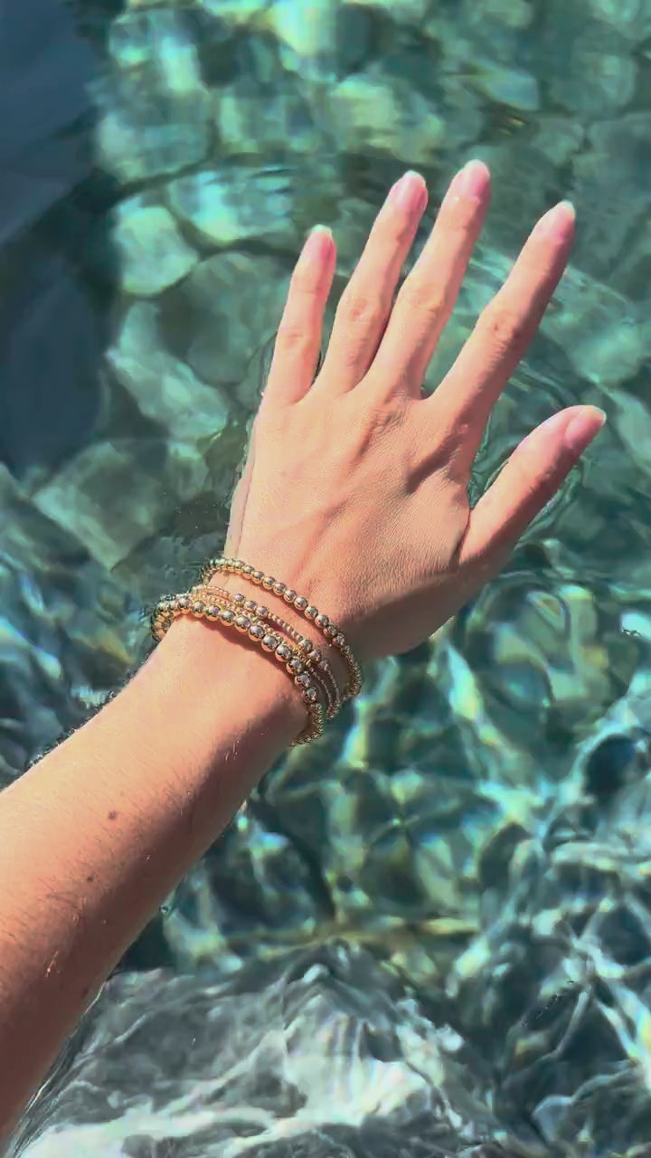 Stack of Steadfast 14k gold-filled bead bracelets worn in clear water